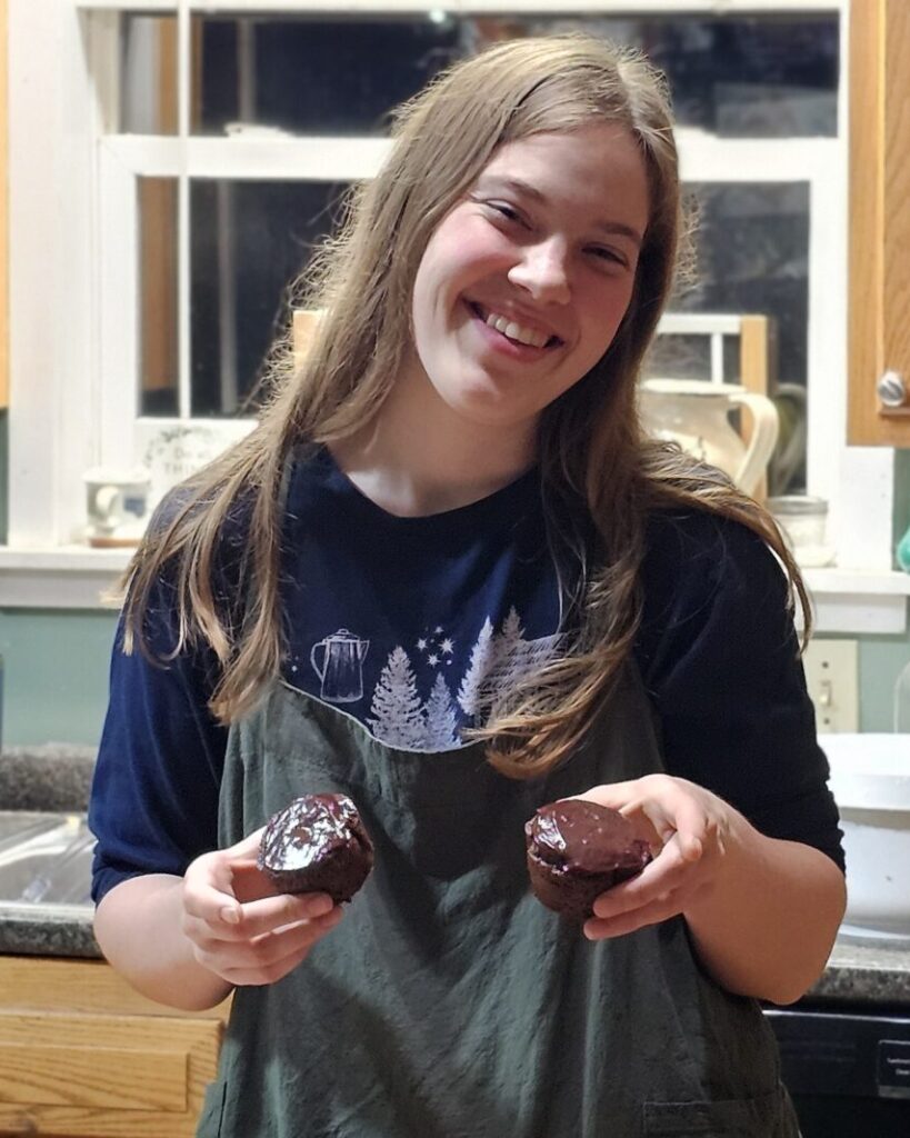 A girl putting chocolate ganache on cupcakes